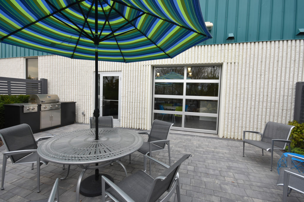 Outdoor patio area of an office with a round outdoor table, chairs, and an umbrella.