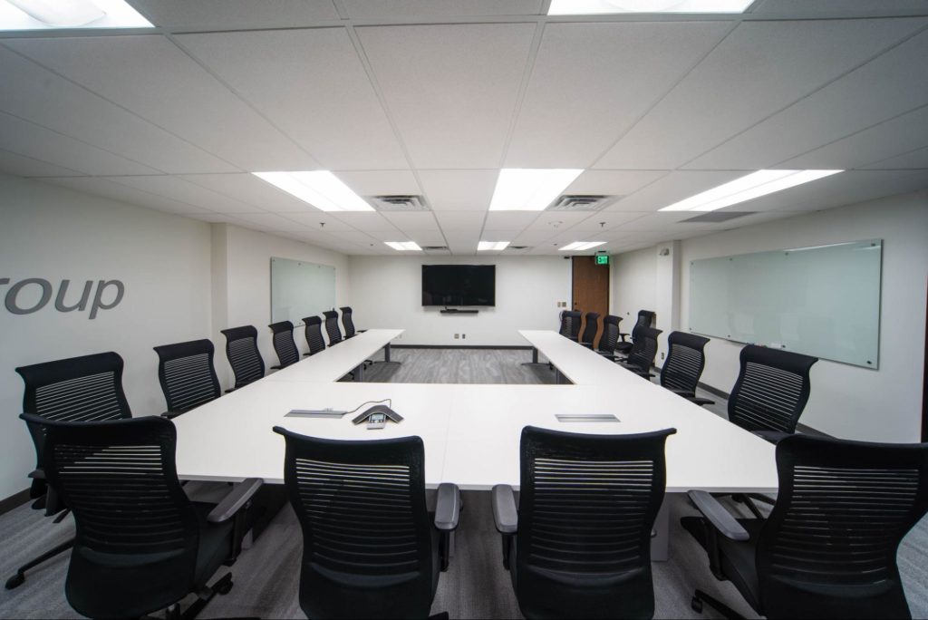 Office conference room with tables and chairs arranged around a TV monitor.