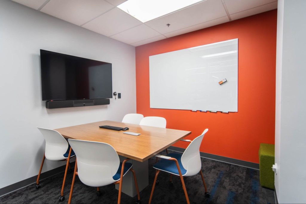 Table and chairs in a meeting room with wall-mounted TV and whiteboard.