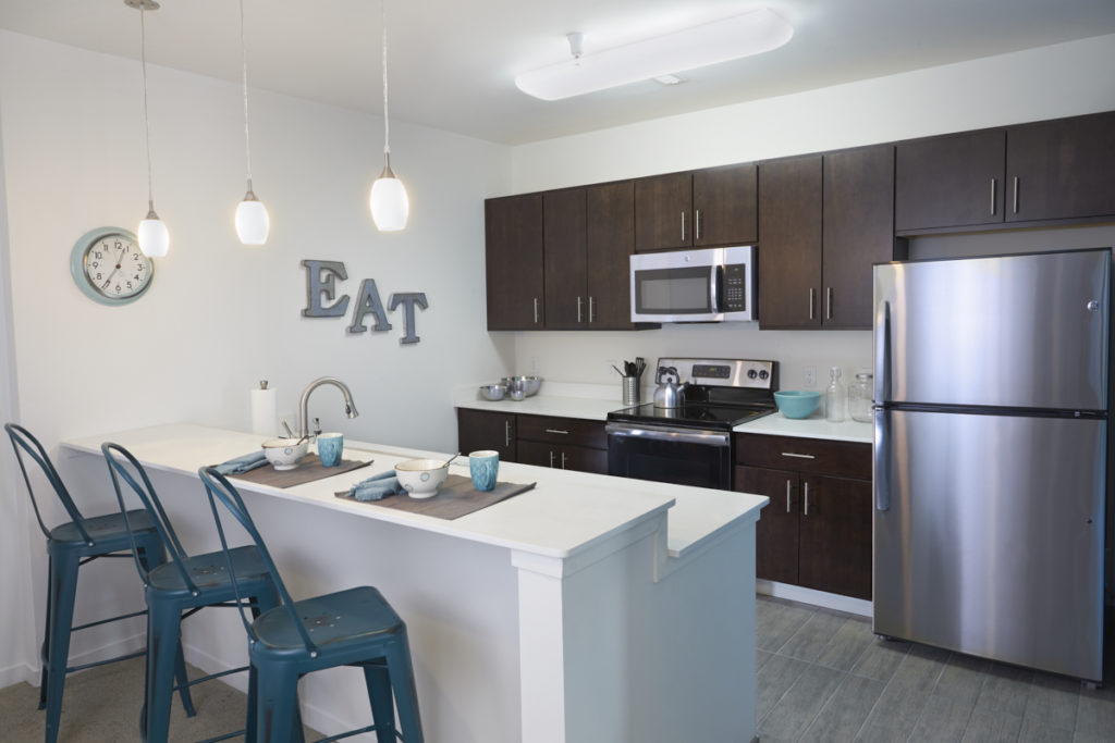 An apartment's kitchen with three blue chairs next to the counter.