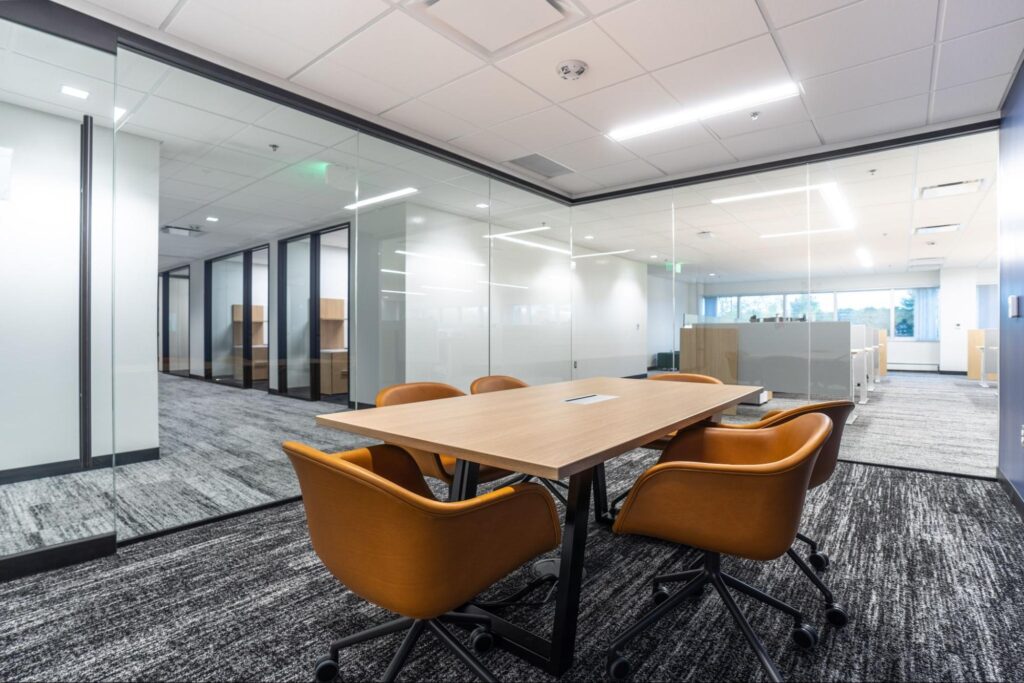 Small conference room with glass walls and orange tables arranged around a wood table.