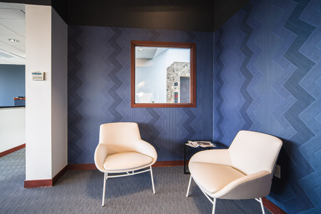 Two white chairs in a small office lounge next to blue walls with a zig zag print.