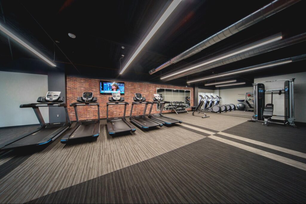 A group of treadmills facing a wall-mounted TV in a fitness center.